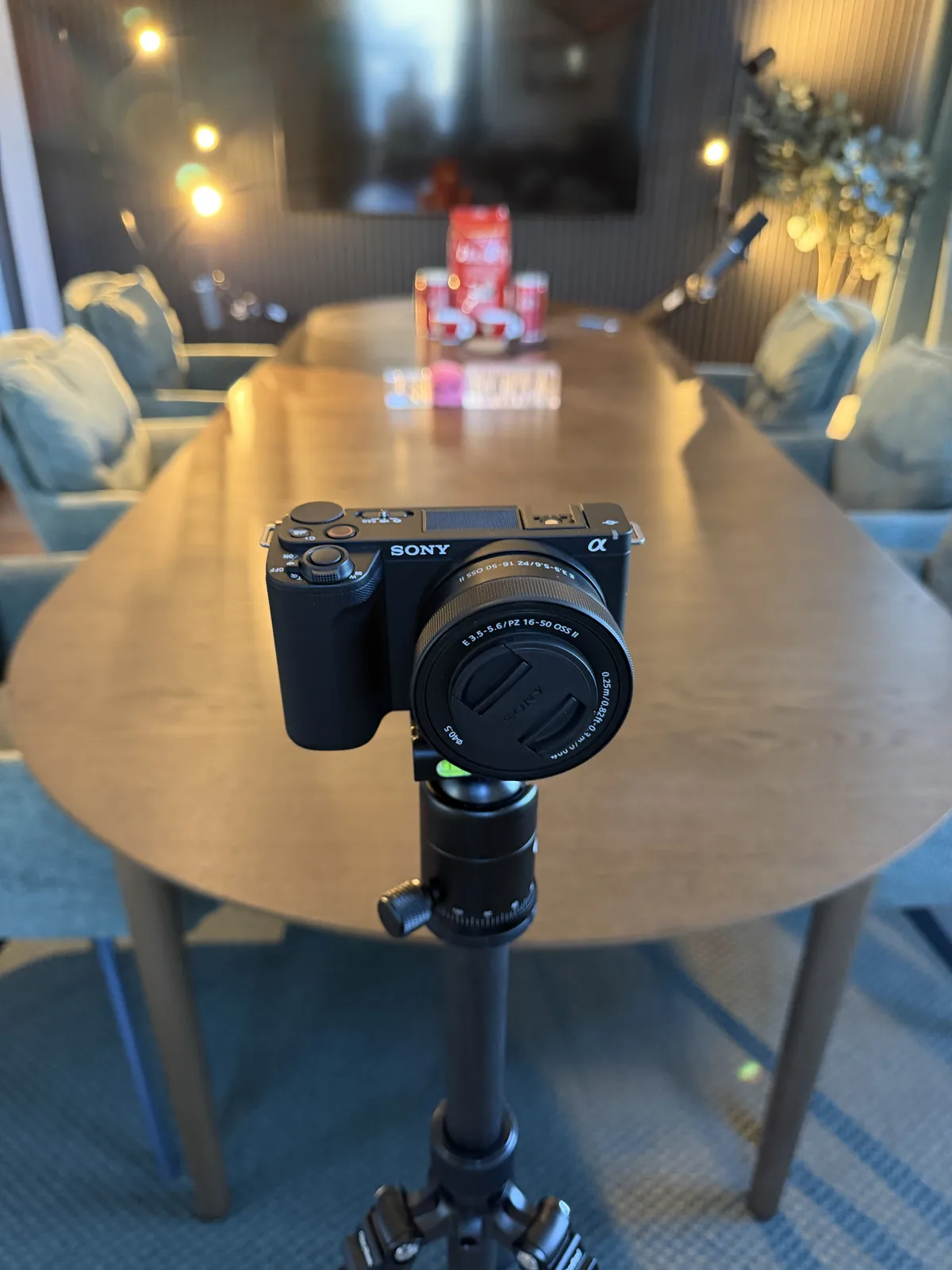Sony ZV-E10 II mit 16-50-mm-Objektiv auf einem Stativ, im Hintergrund unscharf der Aufnahmetisch und die Akustikwand