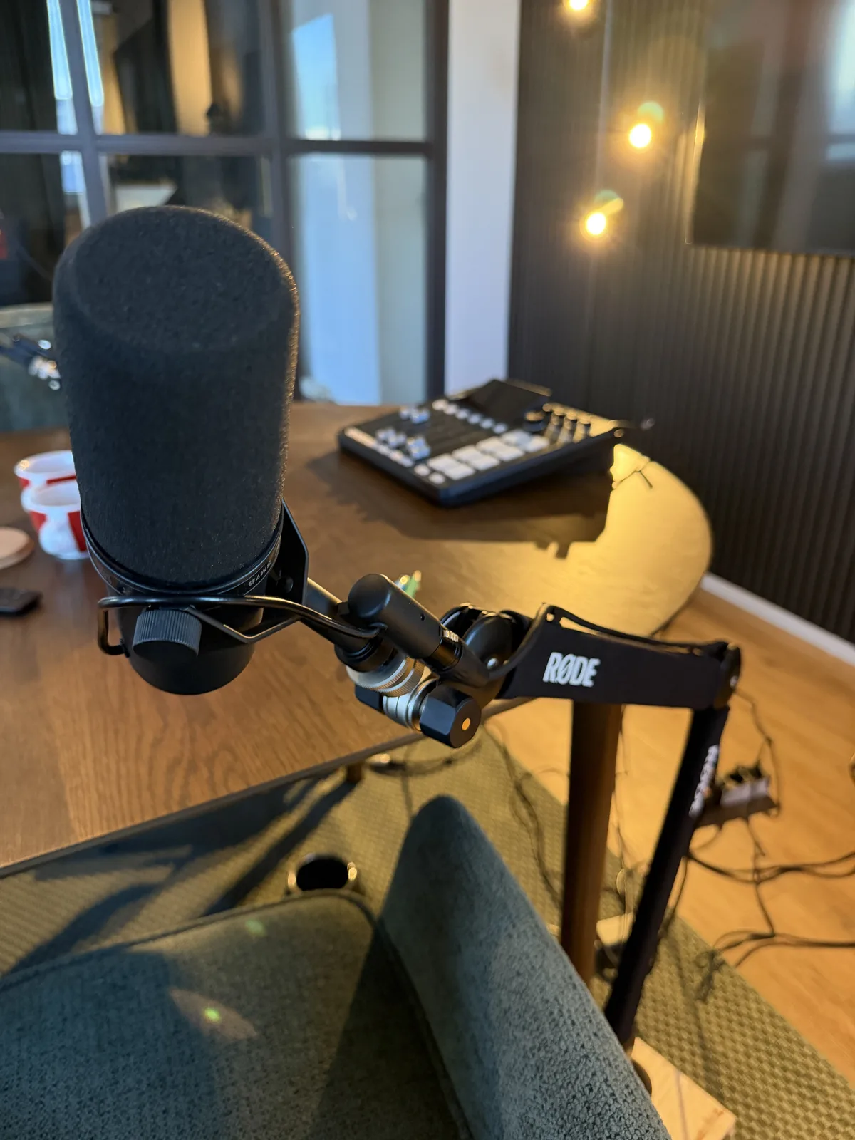 Shure SM7B mit Schaumstoff-Windschutz in der Spinne, montiert an einem schwarzen RØDE-Schwenkarm über dem Holztisch
